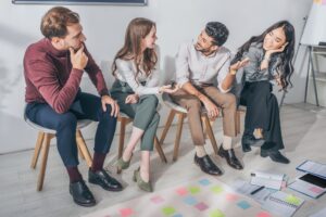 happy multicultural coworkers sitting on chairs in office