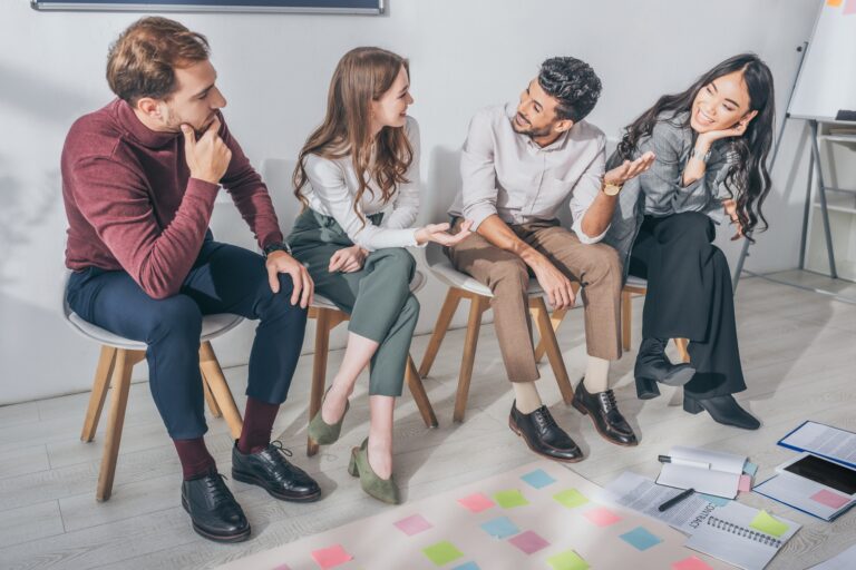 happy multicultural coworkers sitting on chairs in office