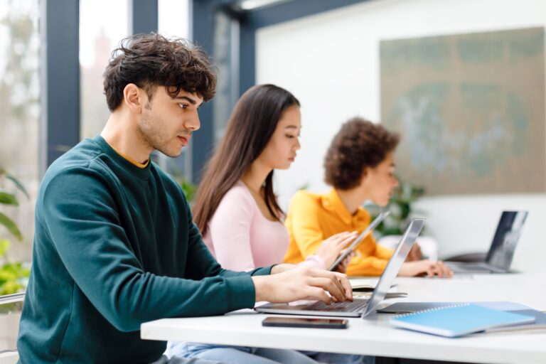 Multiracial male and female students studying for test, making homework with gadgets, focused guy