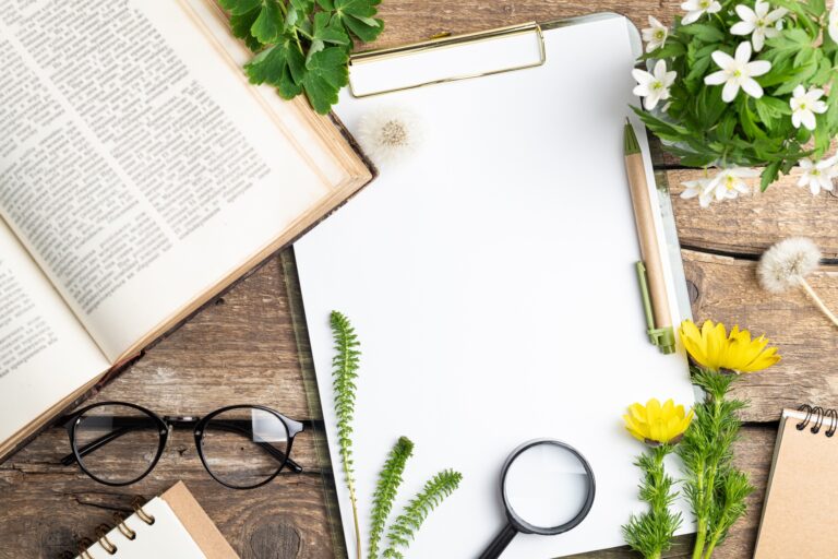 White blank, book, flowers, plants, magnifier on wooden background. Ecology, botany, zero waste