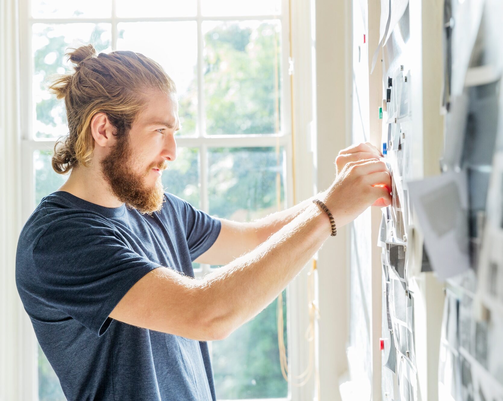 Young male designer pinning mood board ideas to wall in creative studio