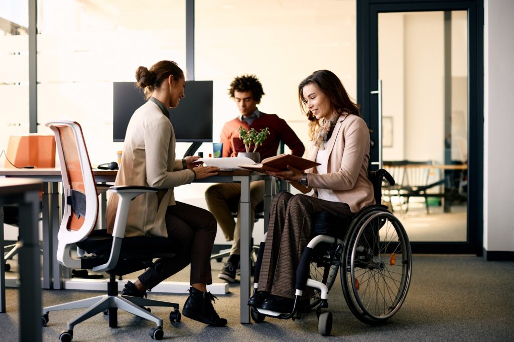 Happy businesswoman in wheelchair going through reports with her colleague in the office.