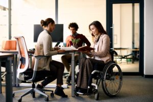 Happy businesswoman in wheelchair going through reports with her colleague in the office.